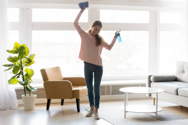 A girl in pink happily dances while tidying up the living room. 