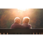 An elder couple sitting together facing the sunset.