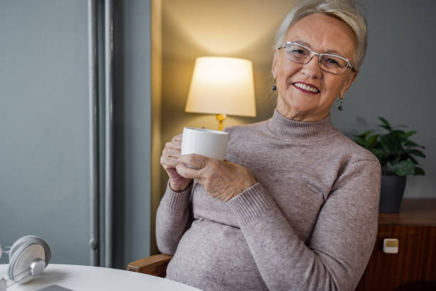 A happy elder woman in a well-lit space holding her cup of tea in the afternoon.