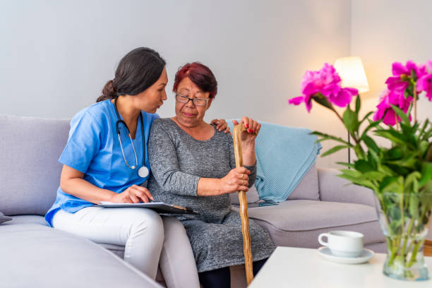 A calm elder woman talking to her caregiver while they're sitting in the living room sofa in the evening.