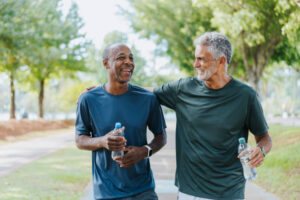 two active senior men holding their bottles of water & enjoying each other's company while walking in the park